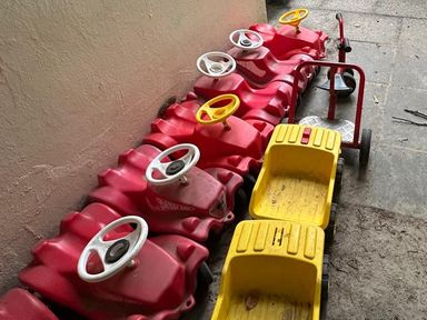 Rote Rutschautos, gelbe Kipper und ein Roller aufgereiht an der Hauswand